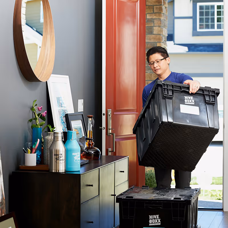 Man carrying a large black Hive Boxx storage container through a doorway into a home.