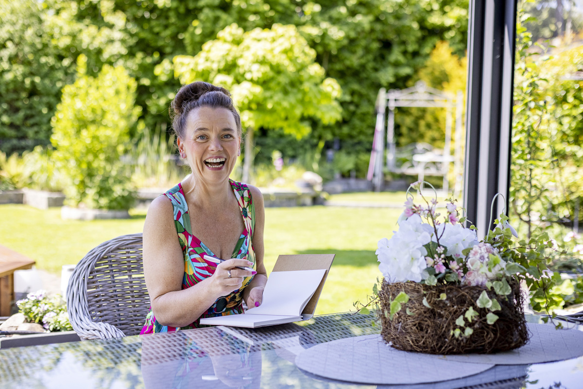 Kati Kreyser lacht beim Schreiben am Gartentisch