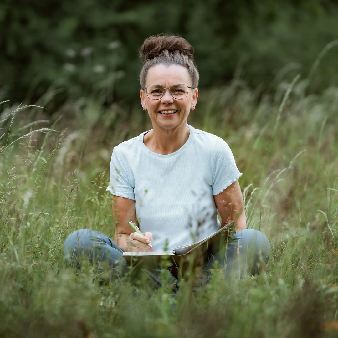 Kati Kreyser sitzt mit Stift und Schreibmappe im Gras