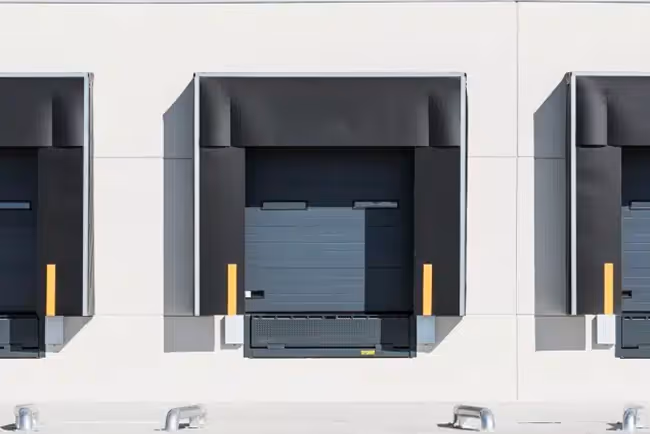 Three closed loading dock doors with black dock shelters on a industrial building facade