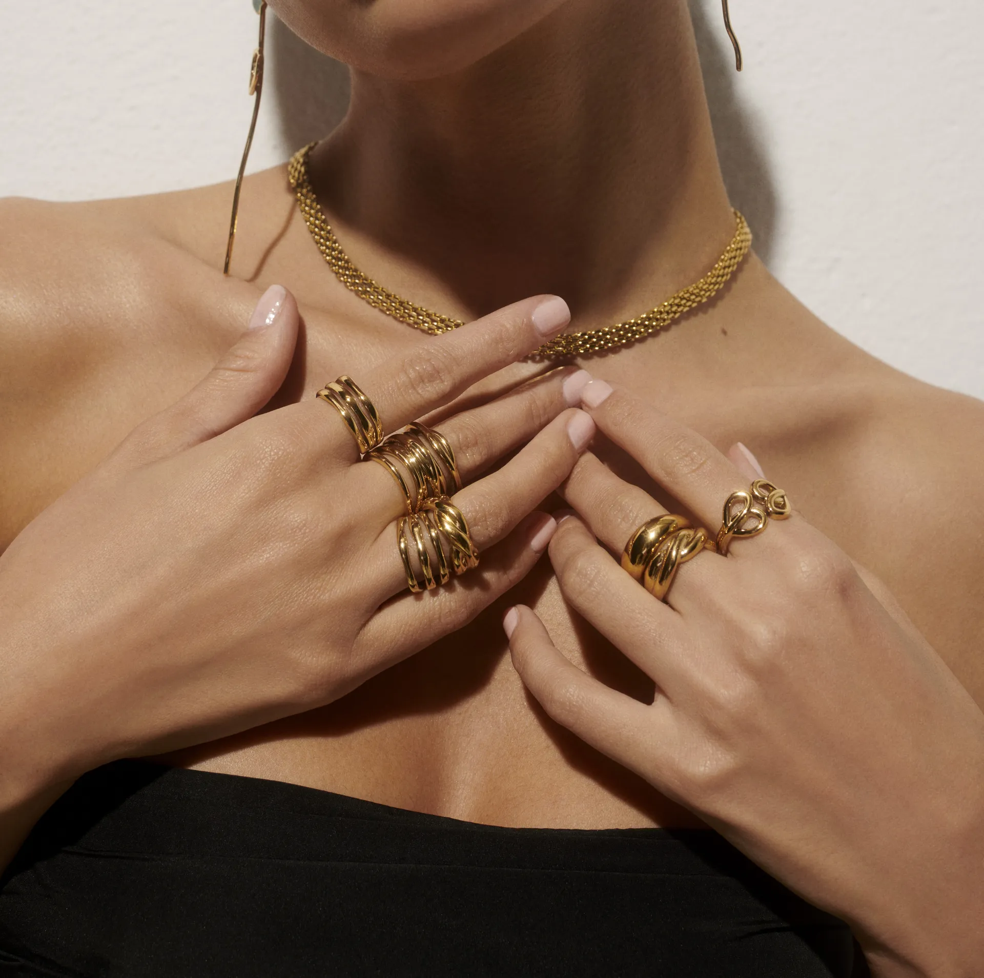 Woman wearing multiple gold rings and a gold chain necklace with a black strapless top