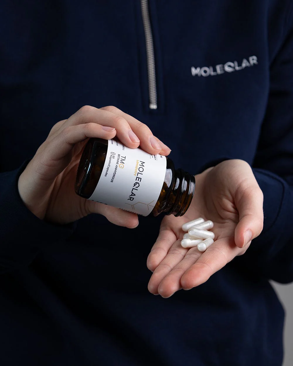 Person in navy blue MoleQlar jacket pouring white capsules from a MoleQlar bottle into their hand