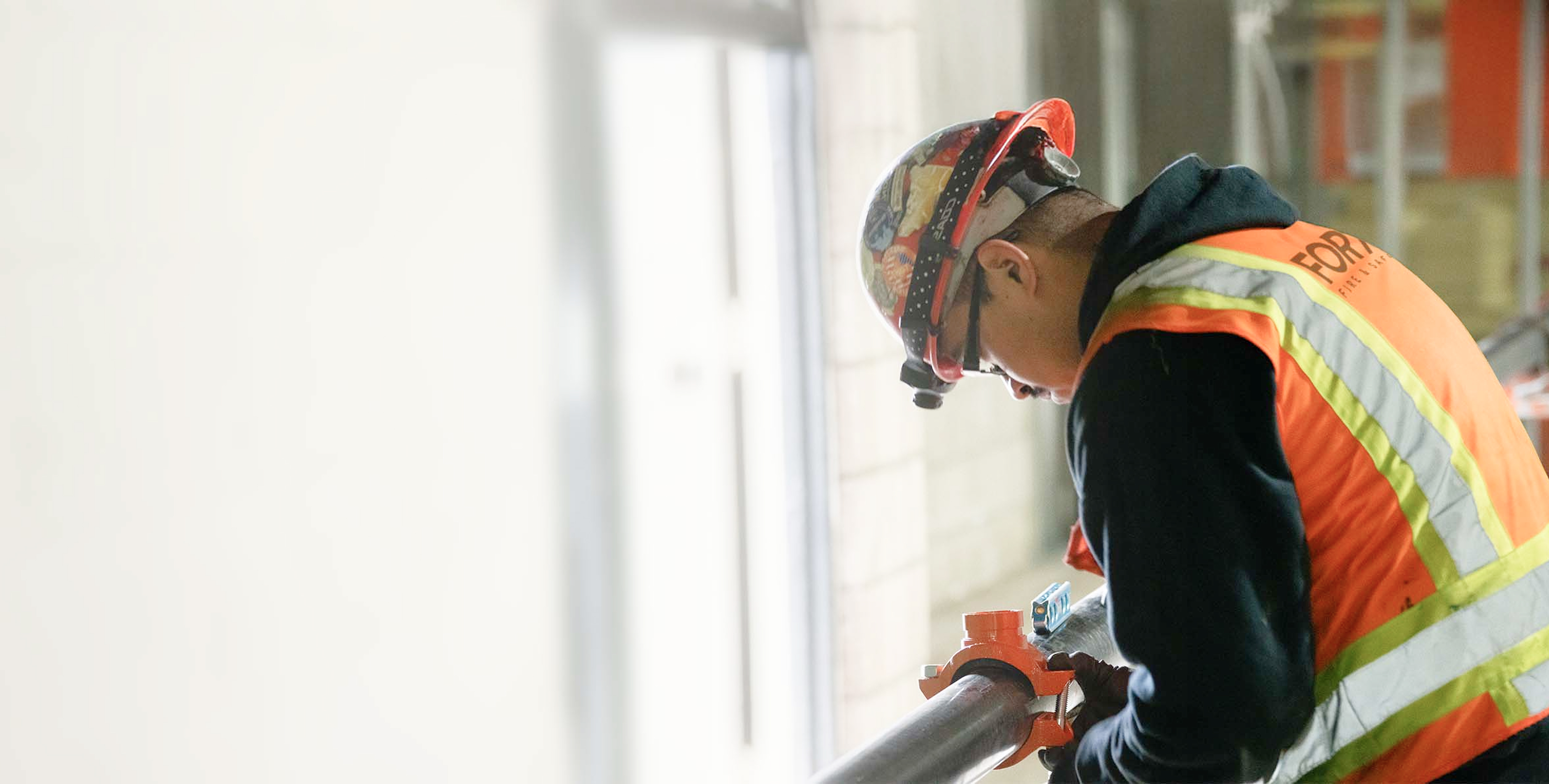 Construction worker in safety vest and helmet inspecting pipe with valve inside a building.