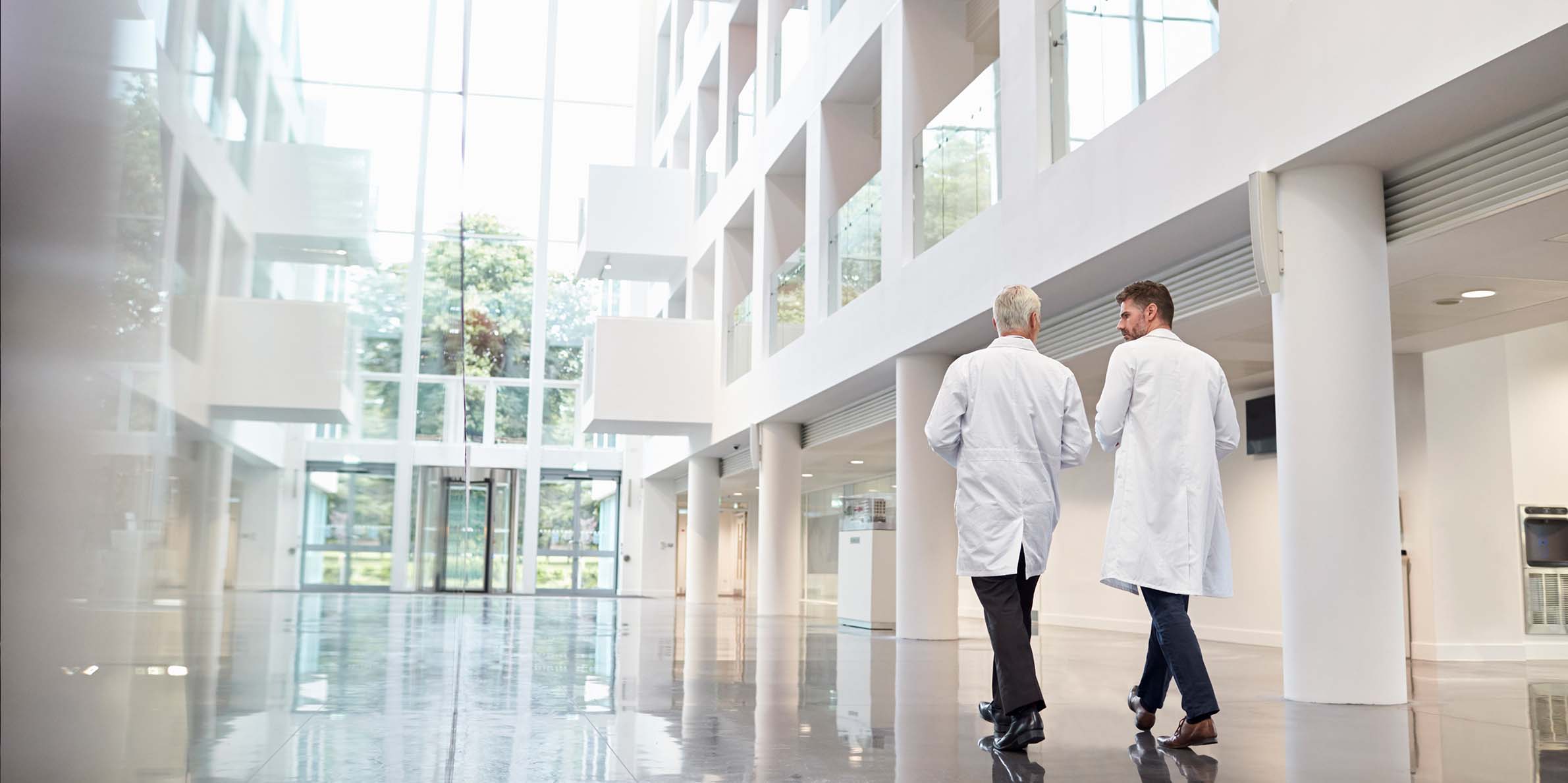 Two doctors in white coats walking and talking in a modern hospital lobby with glass walls.