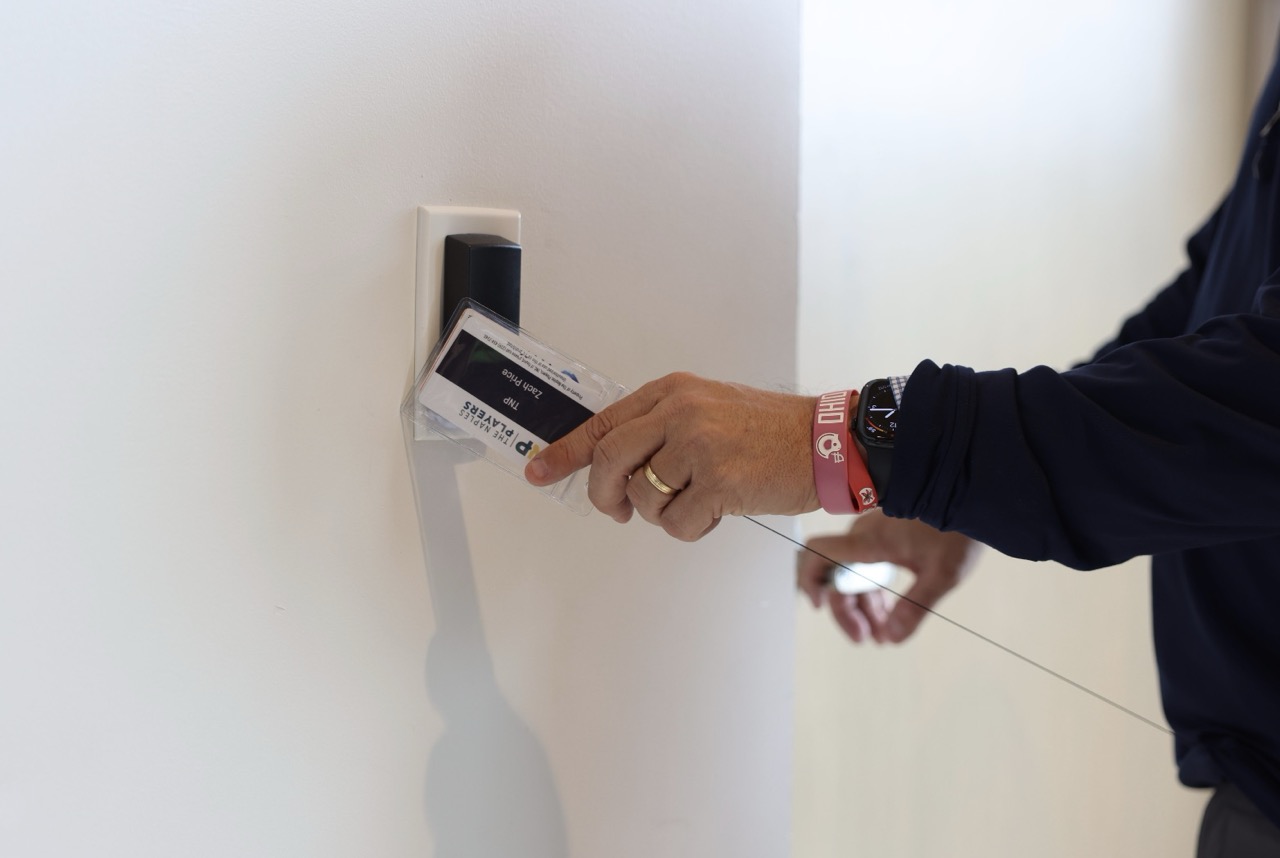 Person holding an ID badge to a wall-mounted card reader for access control.