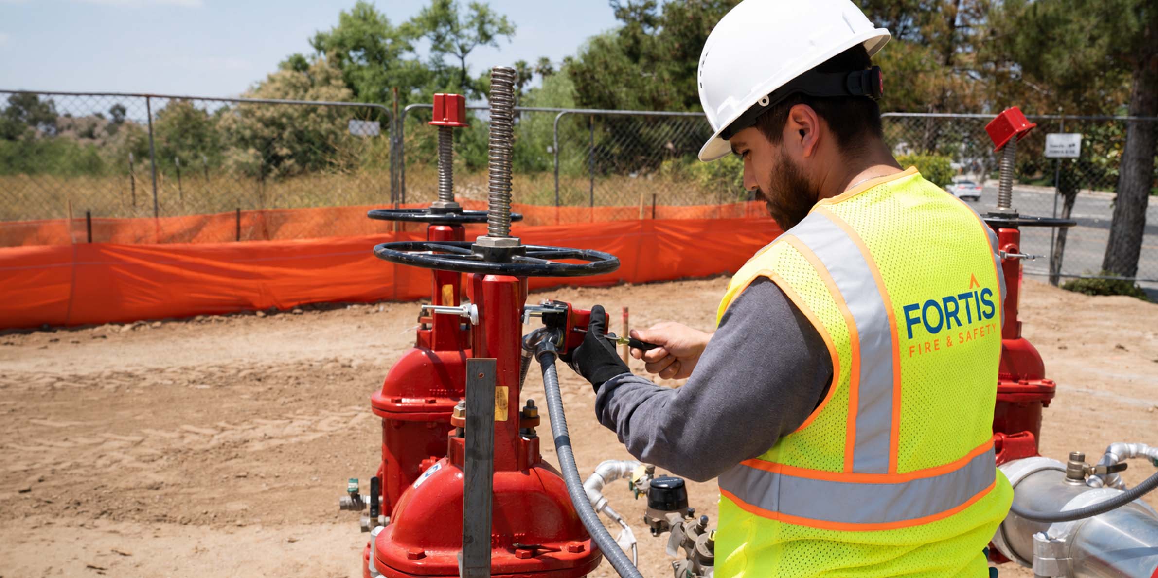 Worker in hard hat and vest adjusts large red fire safety valves at an outdoor construction site.