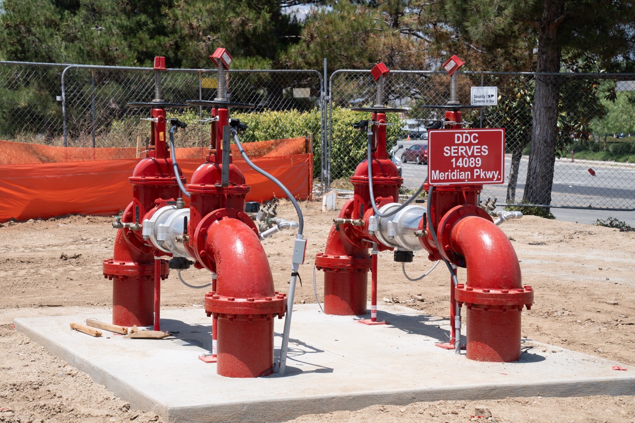 Four large red fire suppression valves installed on a concrete pad at a construction site.