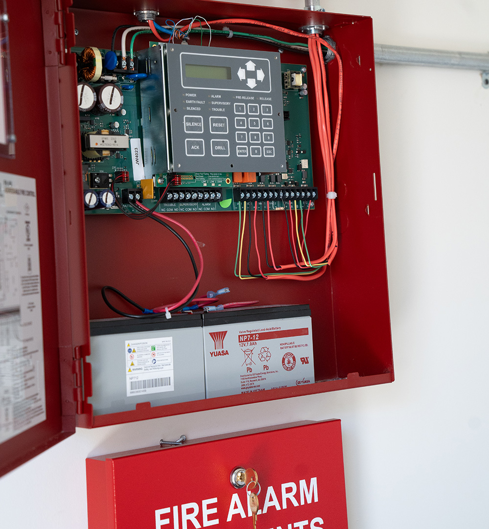 Open red fire alarm control panel showing internal wiring, circuit board, and batteries.