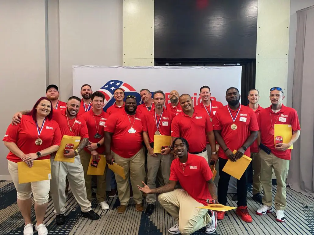 Group of people wearing red shirts with medals and envelopes posing for a photo indoors.