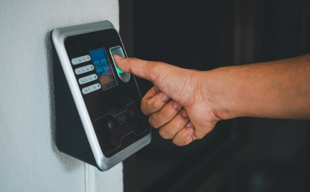 Hand placing finger on a fingerprint scanner for access control on a wall-mounted device.