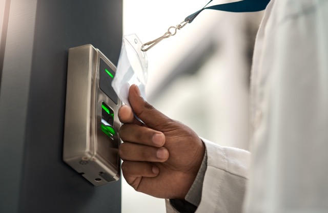 Person using fingerprint scanner with ID card on a security access device.