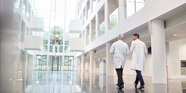 Two doctors in white coats walking and talking in a bright modern hospital lobby.