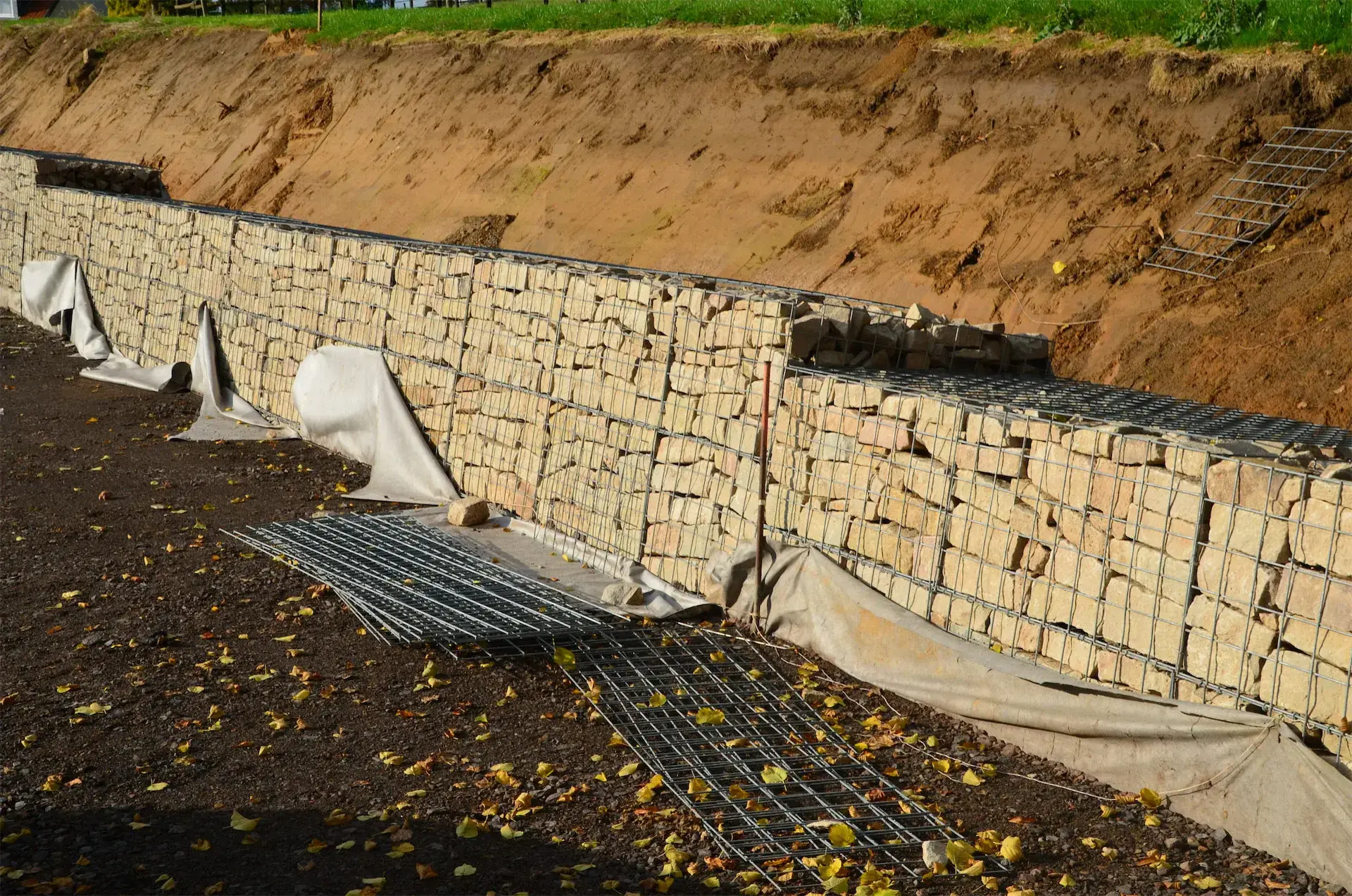 Mur de soutènement en gabions rempli de pierres, en cours de construction sur un talus en terre.