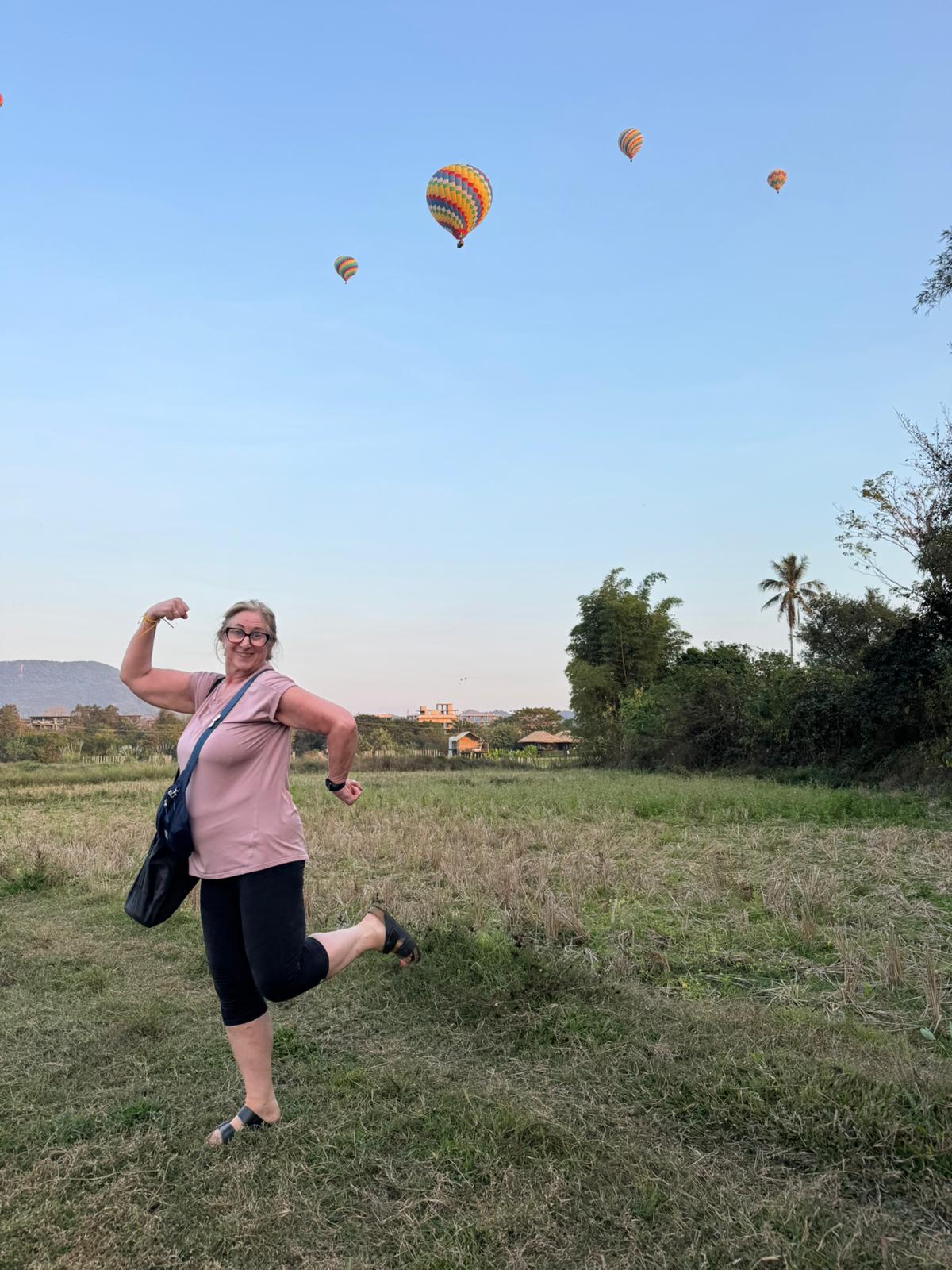fun retiree in active wear with hot air balloons behind her in field