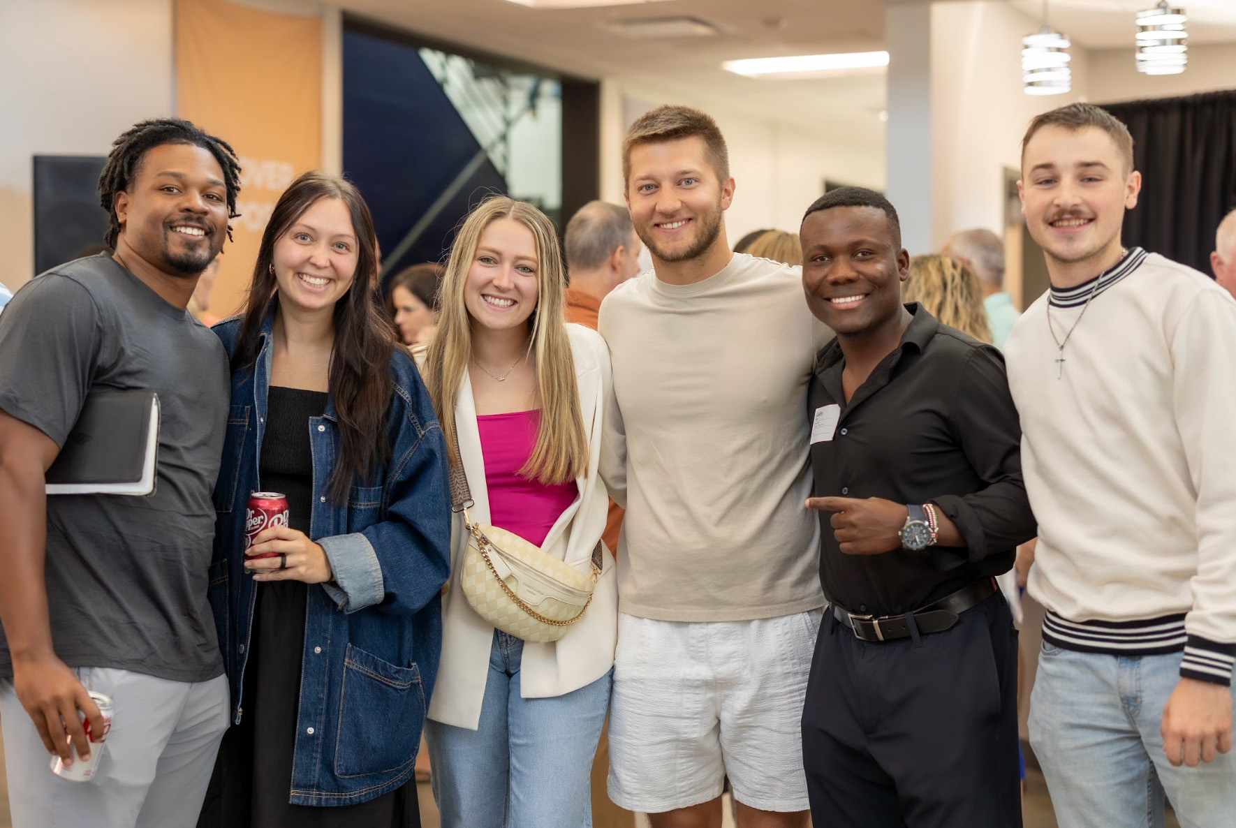 Group of six diverse young adults smiling and posing indoors at a social event.