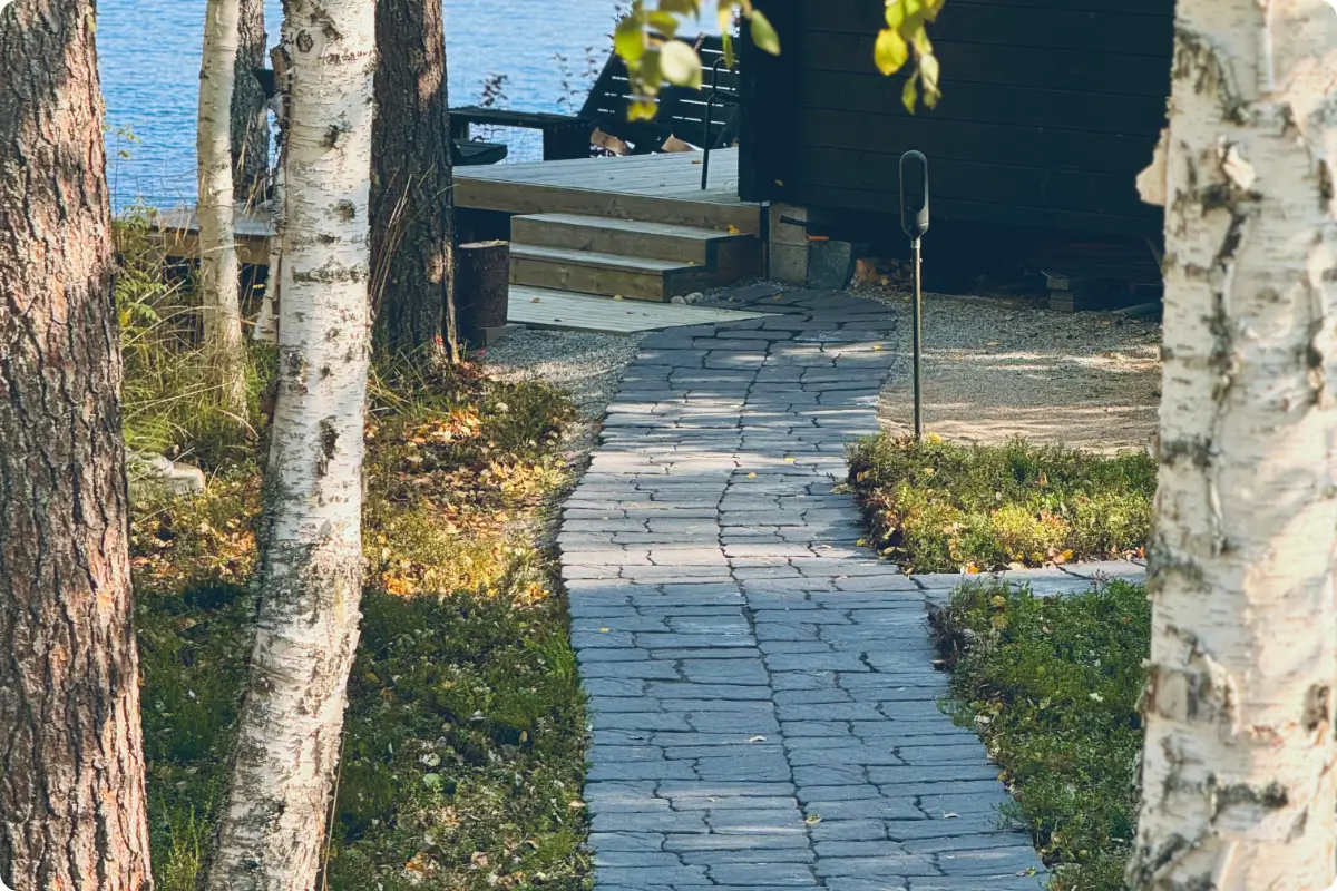 Kalliokivi‑laatoista tehty kulkupolku mökkipihassa, joka kaartuu luonnollisesti ilman millintarkkaa ladontaa.