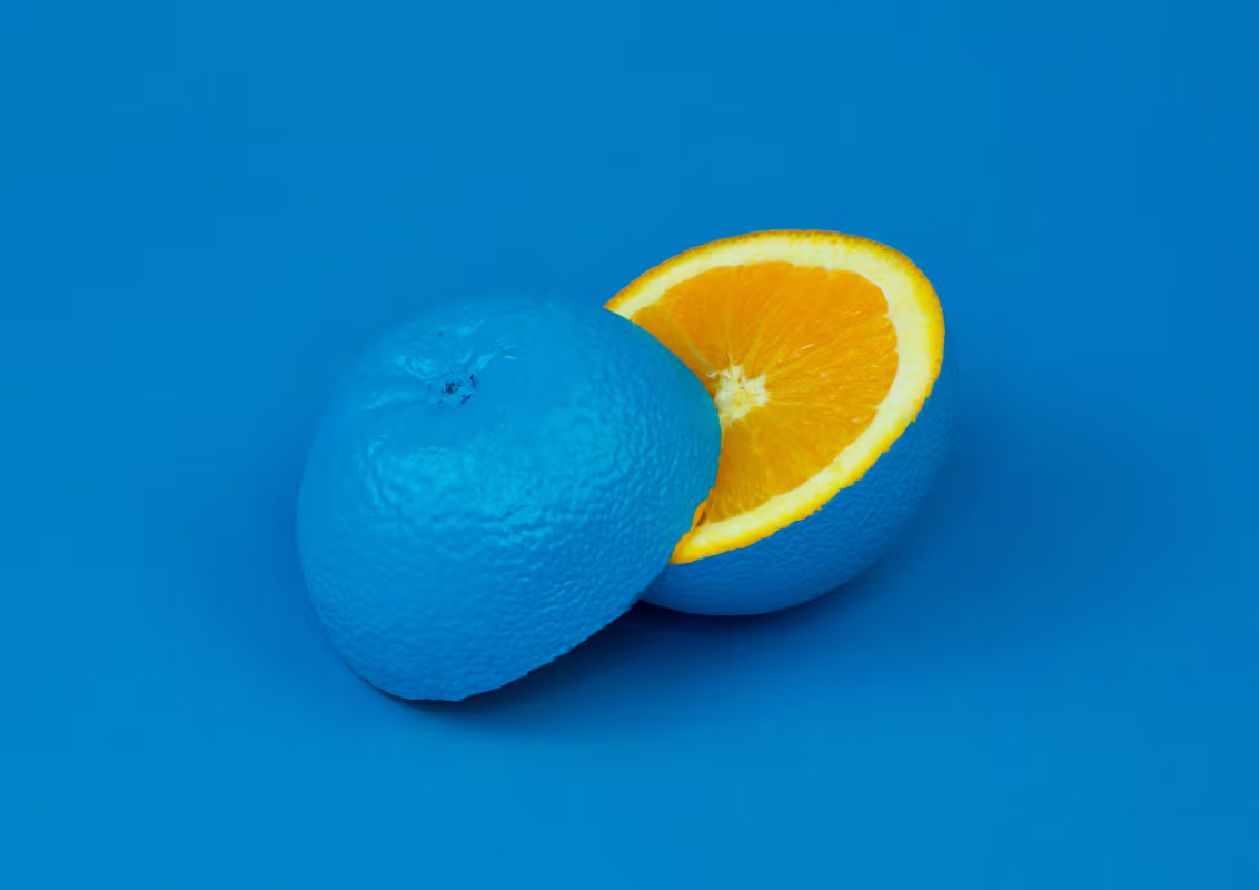 Orange fruit with the peel painted blue and one half cut open showing the natural orange inside on a blue background.