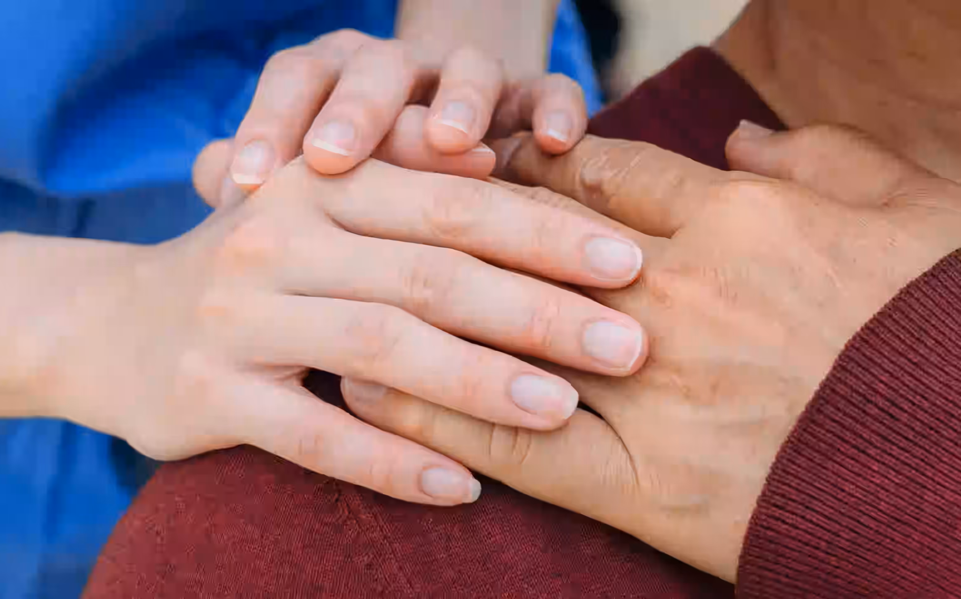 Close-up of two hands gently holding each other, one resting on a shoulder with a maroon sweater.