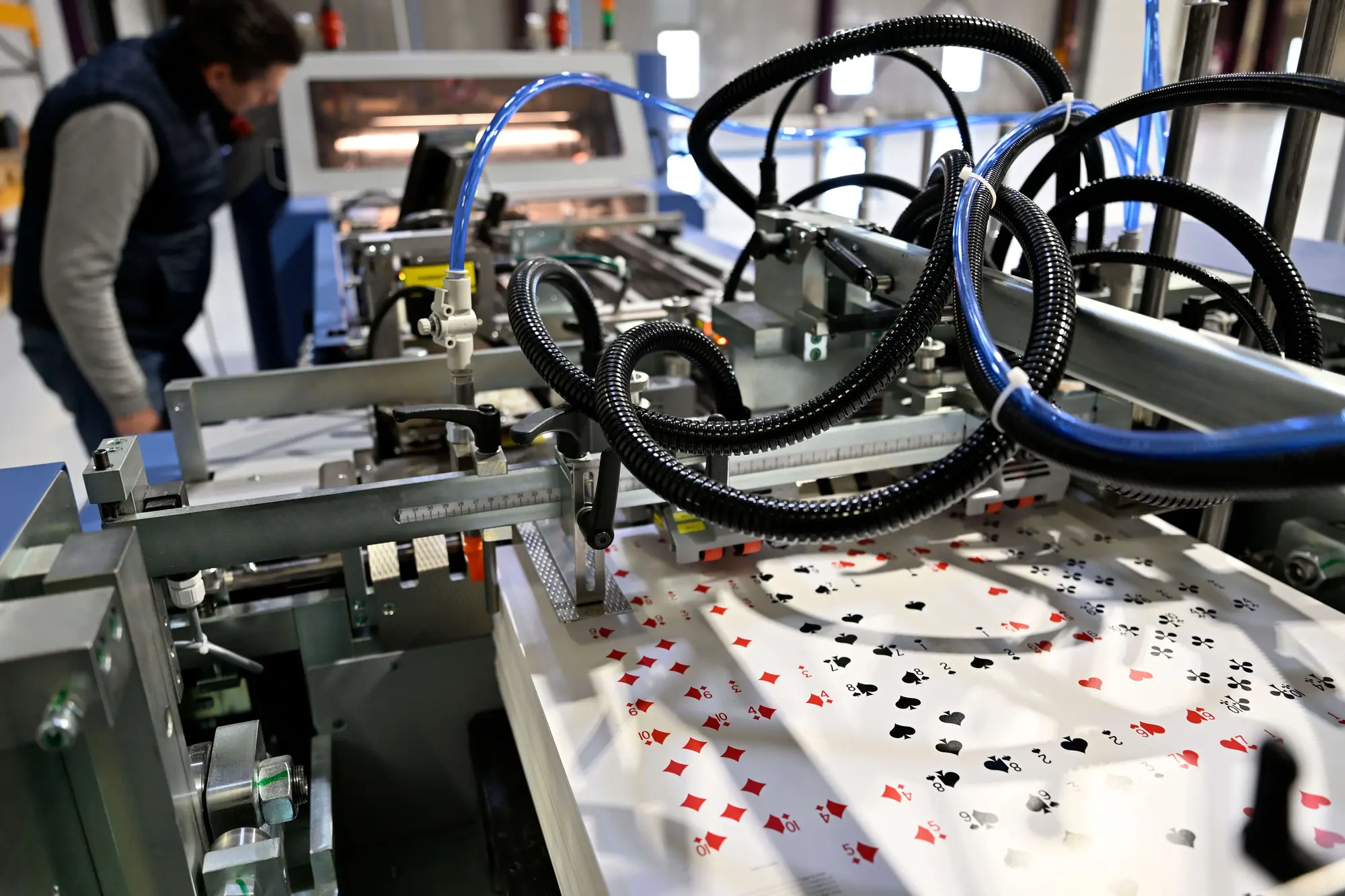 Machine industrielle imprimant des motifs de cartes à jouer sur de grandes feuilles blanches.