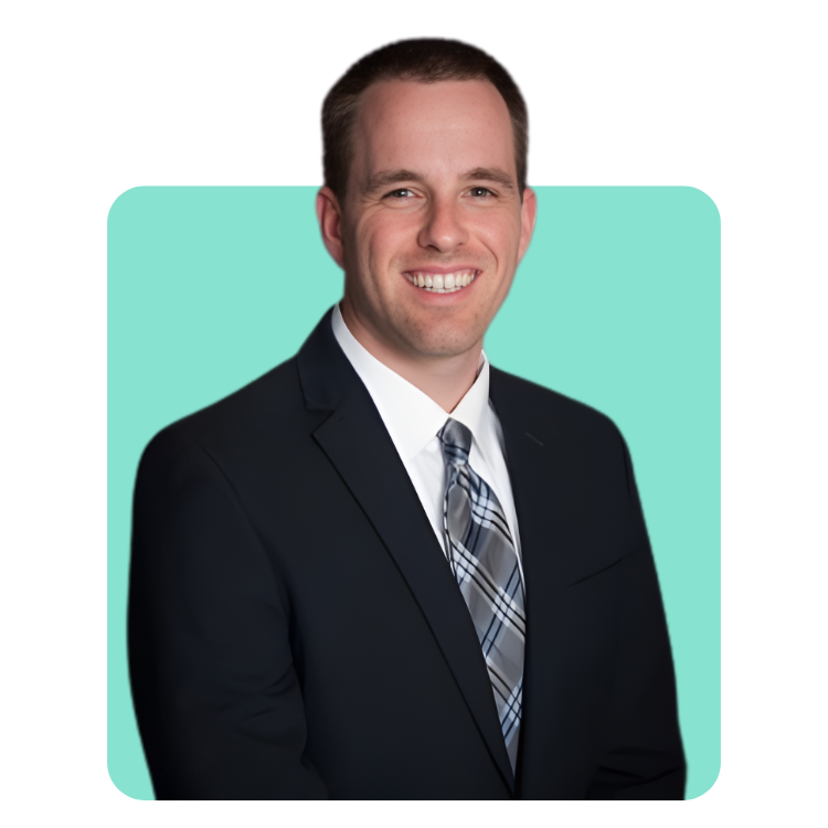Smiling man in a dark suit with a white shirt and plaid tie against a light teal background.