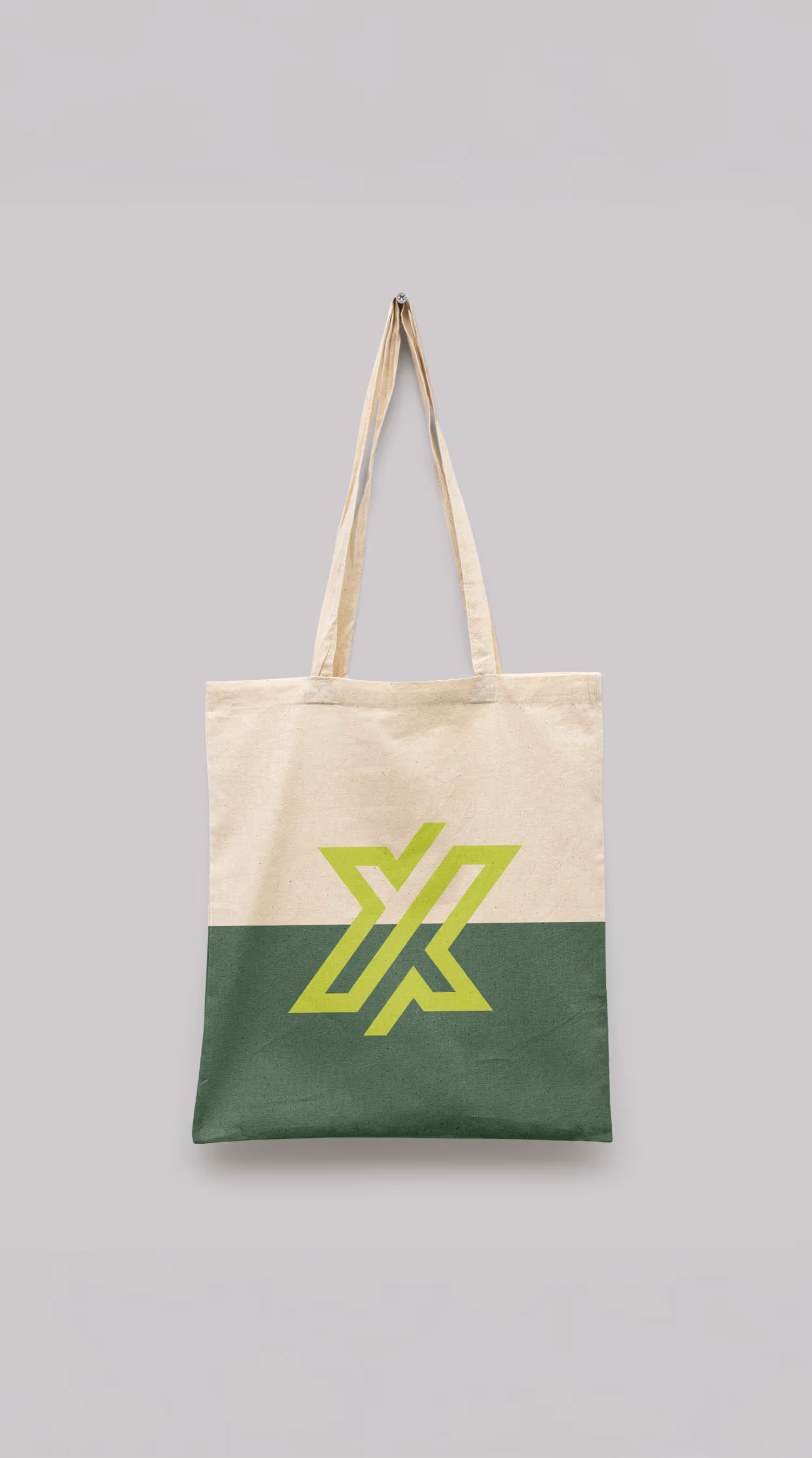 Beige canvas tote bag with dark green bottom half and a large lime green geometric X logo in the center.