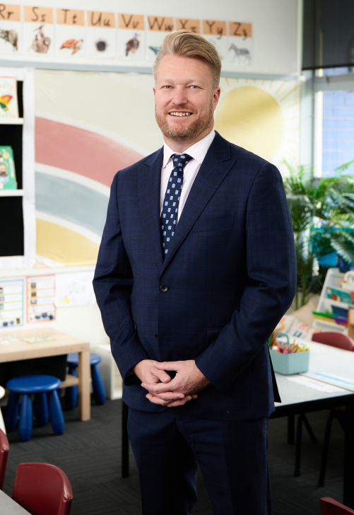 Dr Jarrod Hingston standing in a classroom with a nice dark blue suit