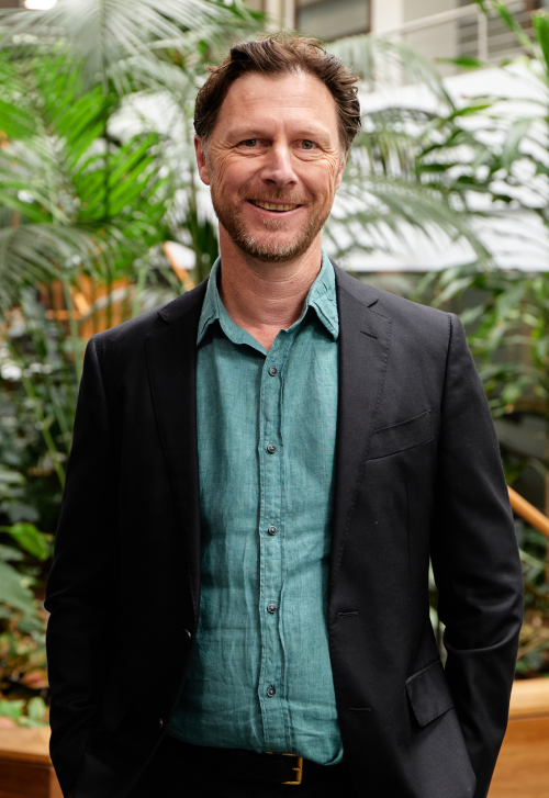 Andrew Cameron posing smiling for photograph in front of an indoor green space atrium