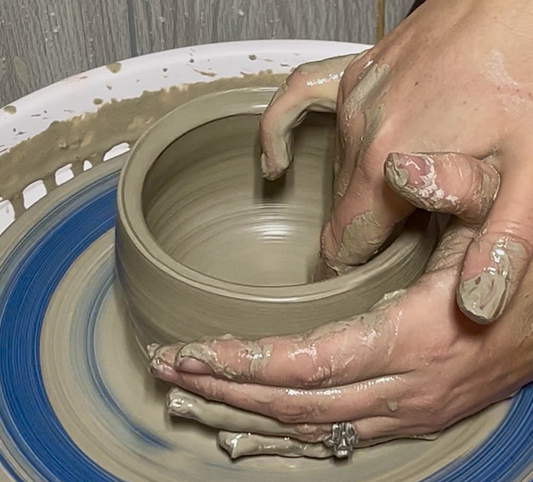 Hands shaping clay on a pottery wheel during Craft Club