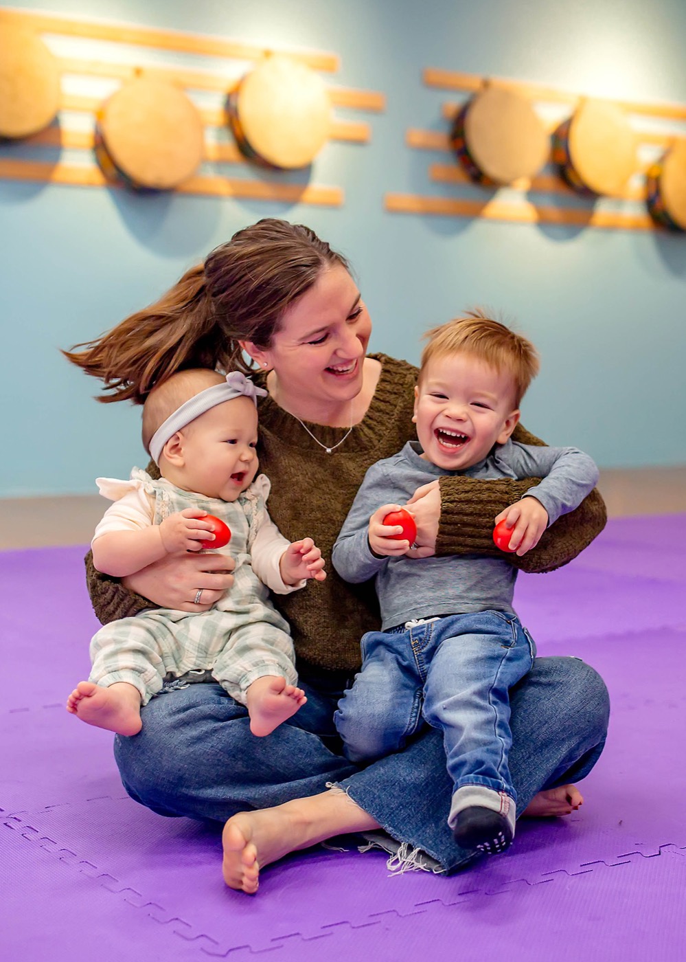 A caregiver making music with a baby and toddler in a Music Together class