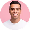 Smiling young man with short dark hair wearing a white shirt against a pink background.
