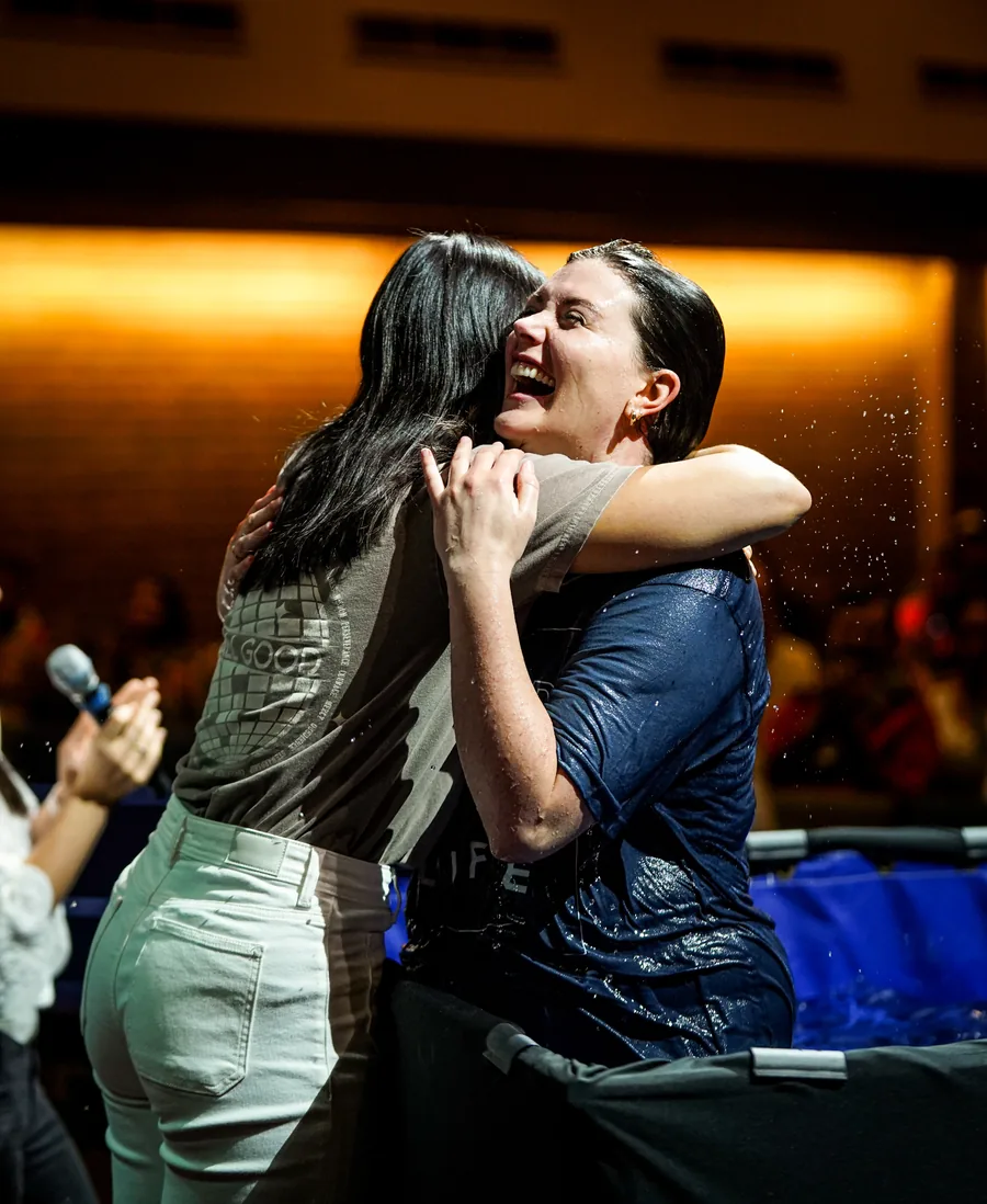 Two women embracing joyfully during a baptism ceremony.