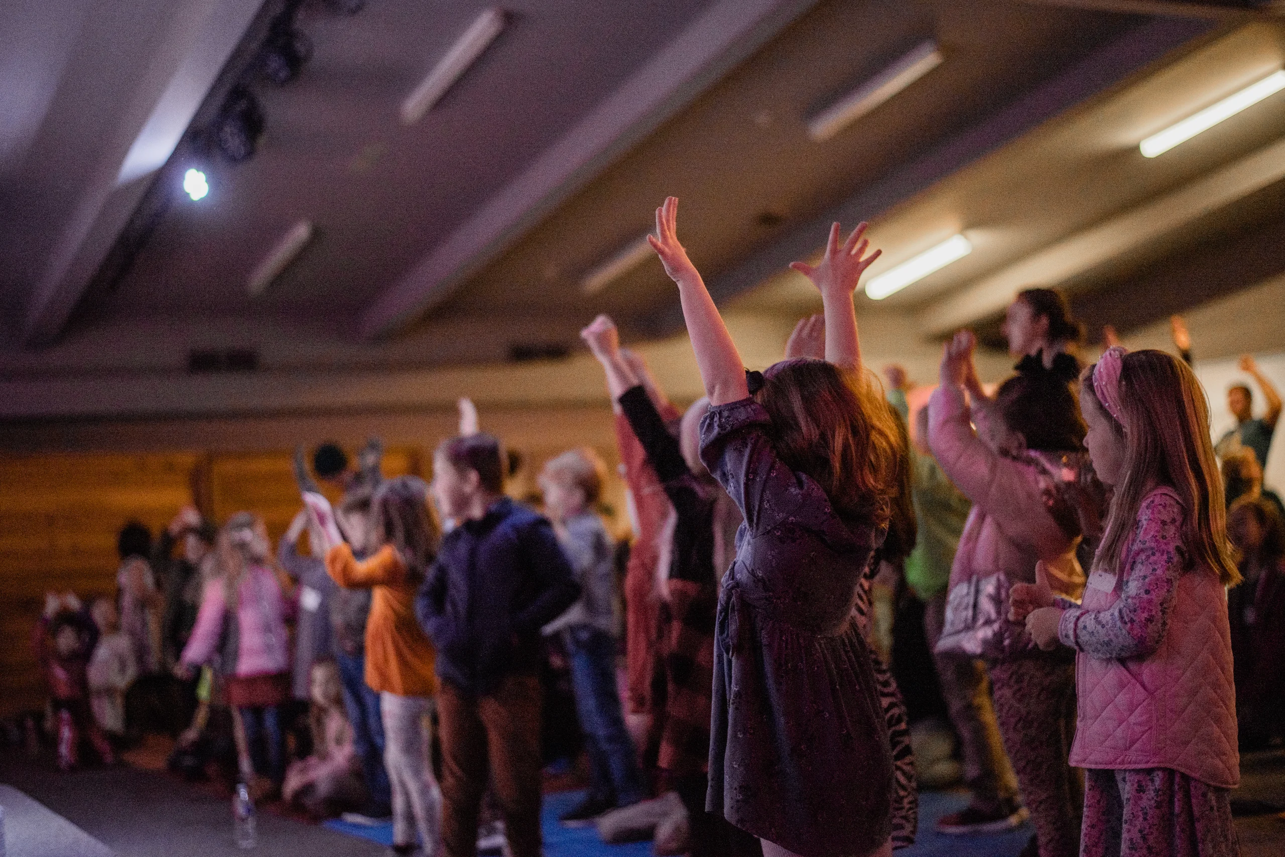 Group of children standing indoors with their hands raised, engaging in an activity.