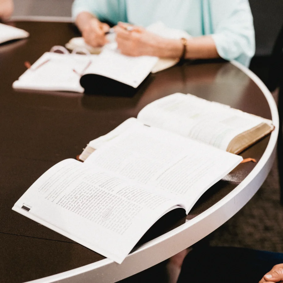Open books on a round table with people studying in the background.
