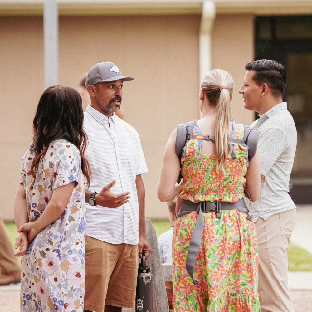 Four adults standing outdoors engaged in conversation.