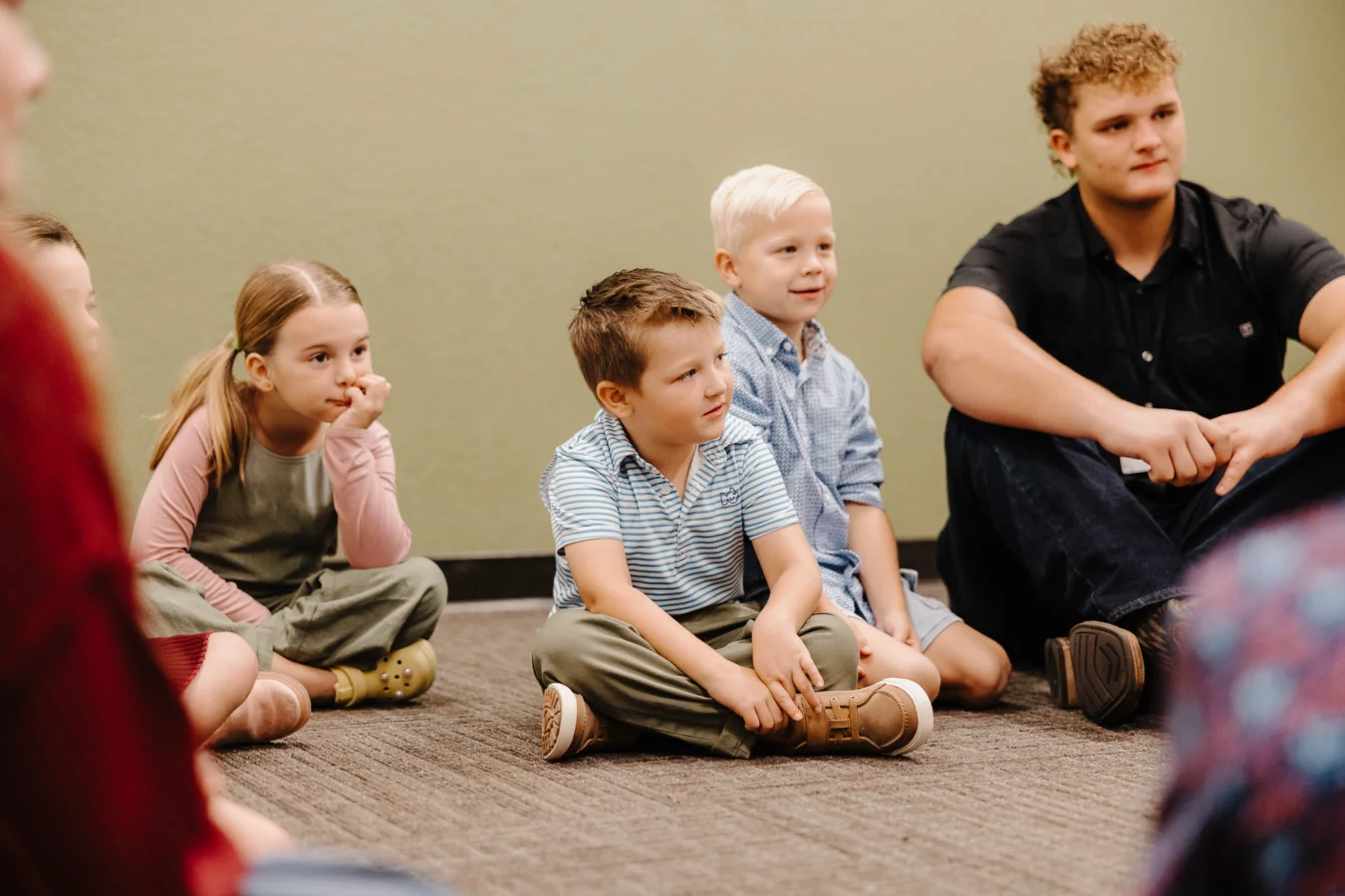 A group of children and an adult sitting in classroom.