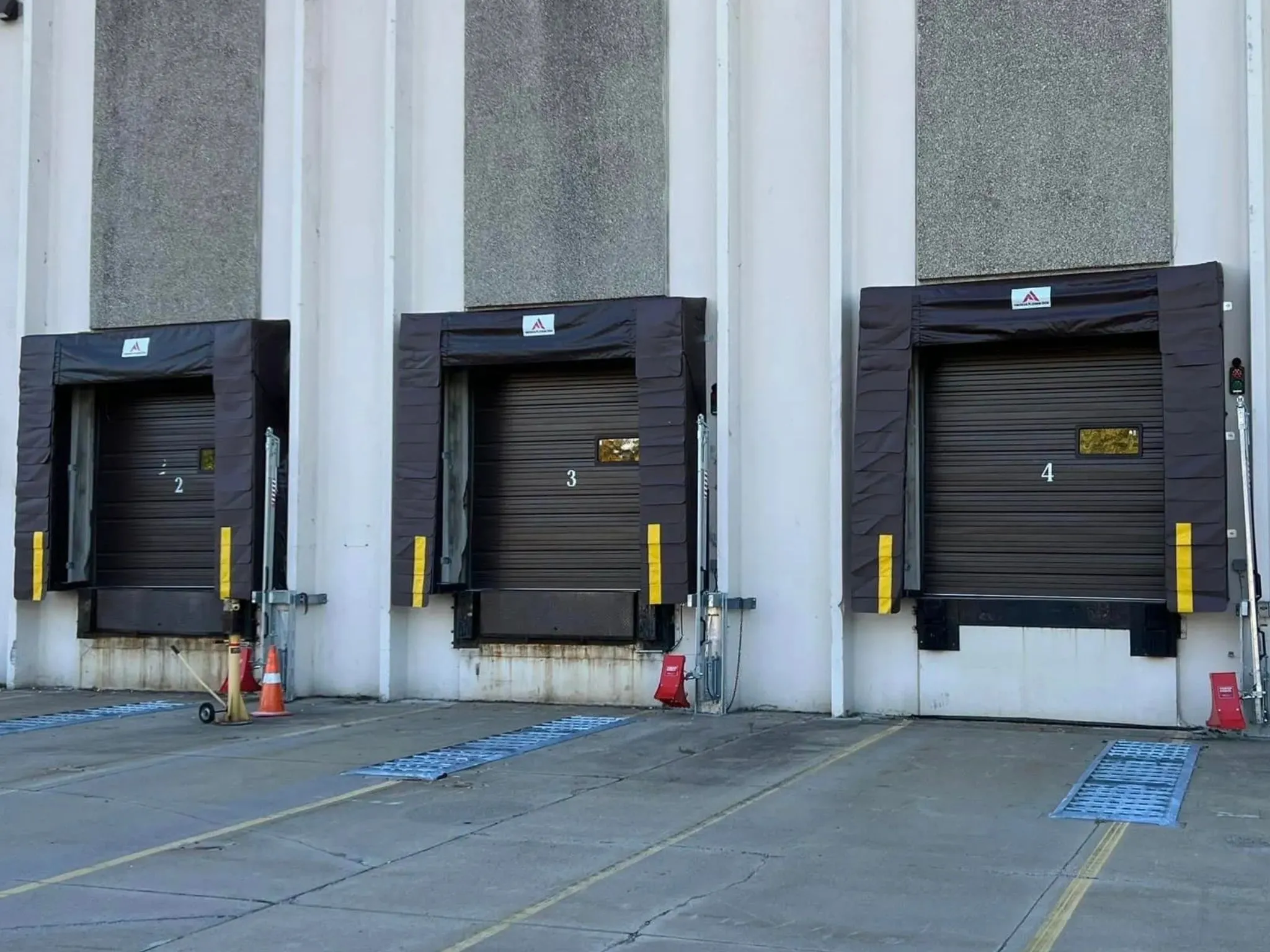 Three numbered loading dock doors with black protective padding and concrete pavement in front.