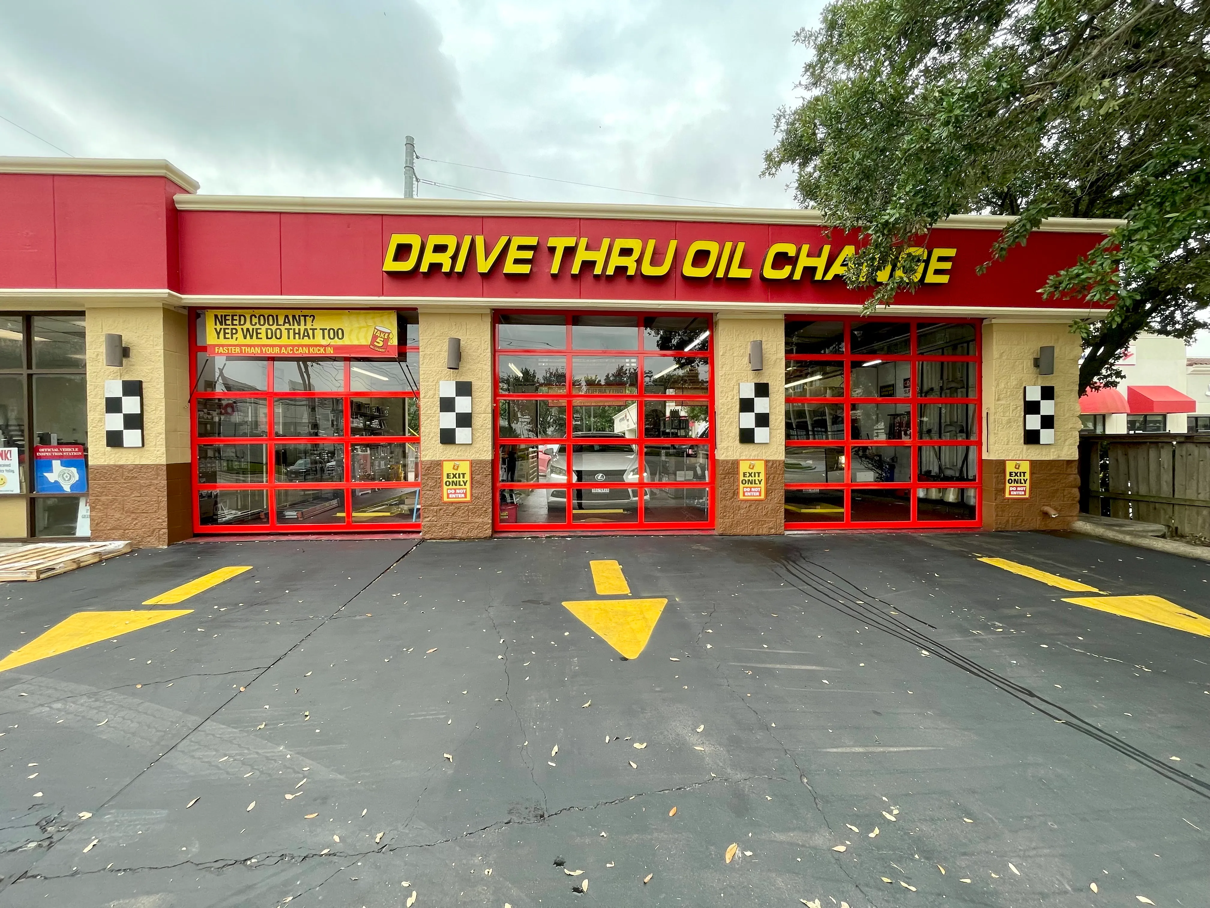 Industrial warehouse interior showing a black pedestrian door within a larger gray commercial rolling door, with lockers and storage along the left wall and an EXIT sign above.