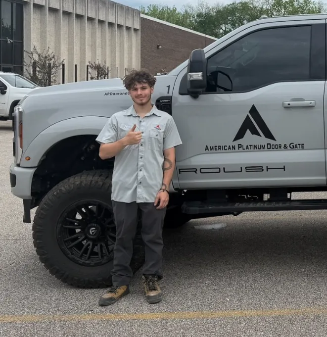 Man giving thumbs up stands beside a gray truck with American Platinum Door & Gate logo.