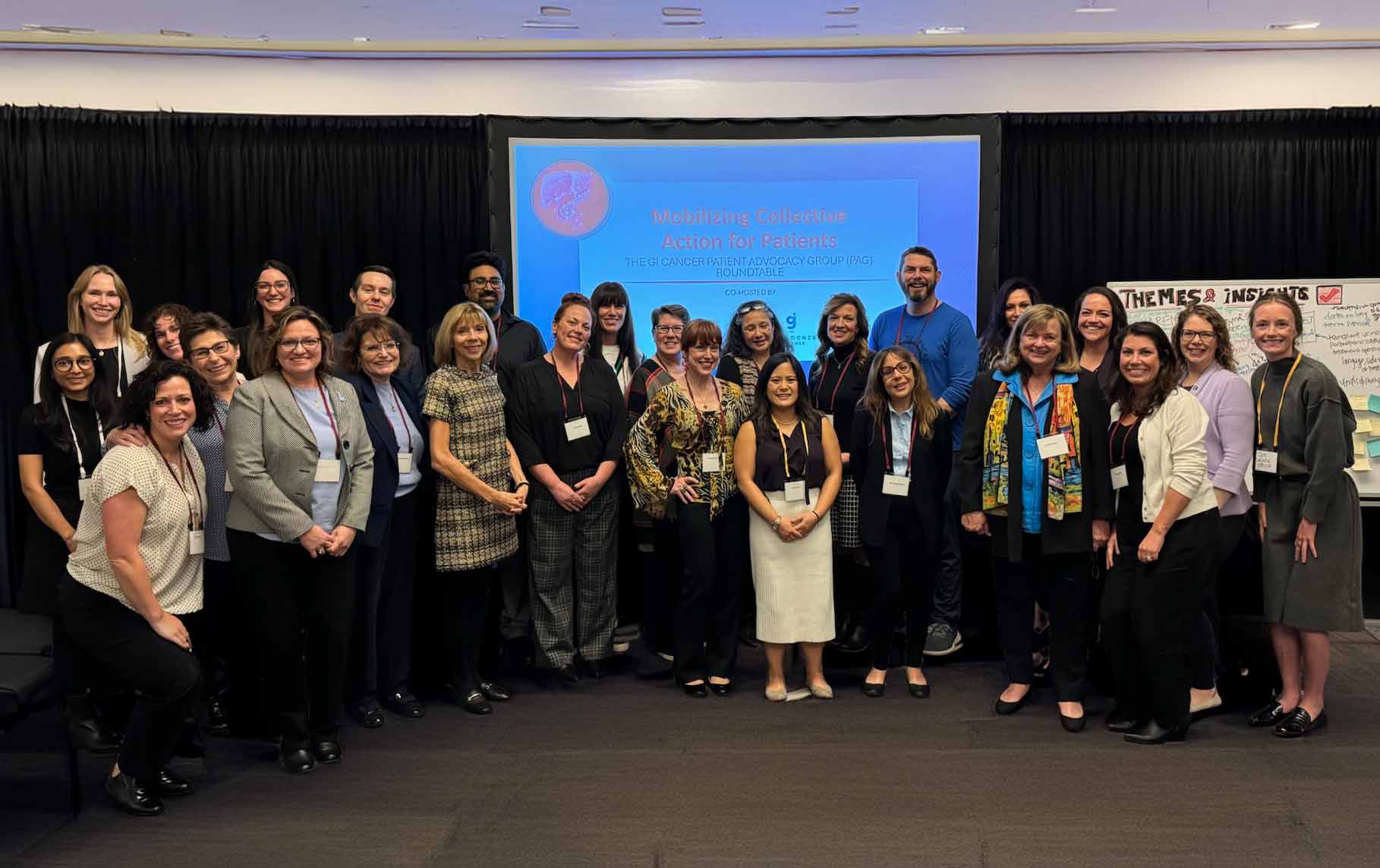 Group of 28 people standing and smiling in front of a presentation screen that reads 'Mobilizing Collective Action for Patients, The GI Cancer Patient Advocacy Group (PAG) Roundtable'.