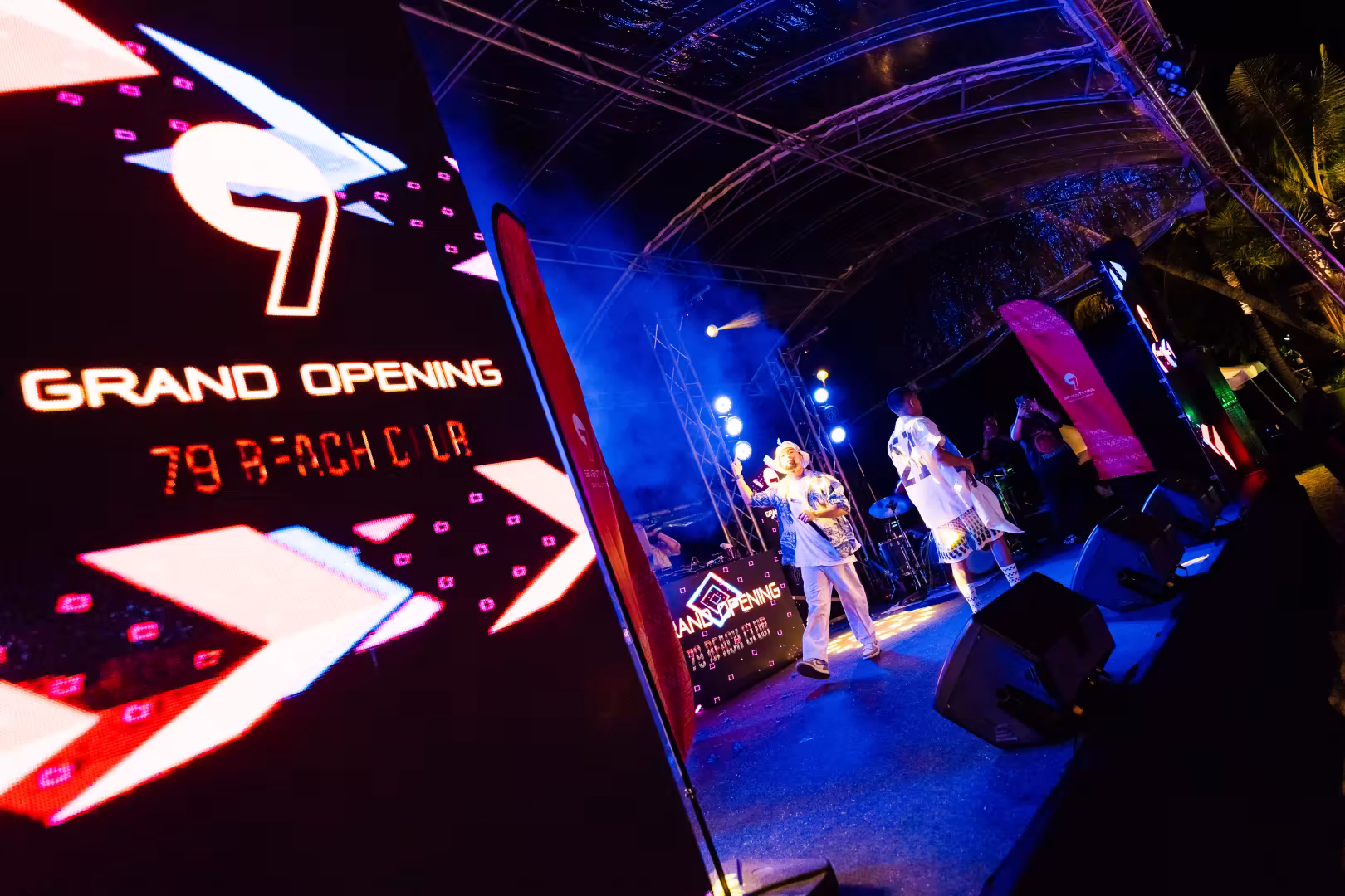 Two performers on stage at the grand opening event for 79 Beach Club under blue stage lights and a transparent tent.