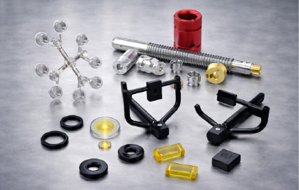 Various metal and plastic mechanical parts arranged on a gray surface, including gears, rings, and cylindrical components.