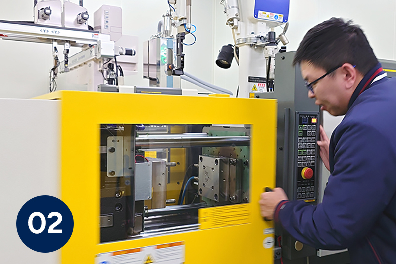 Technician operating a yellow injection molding machine in an industrial setting.
