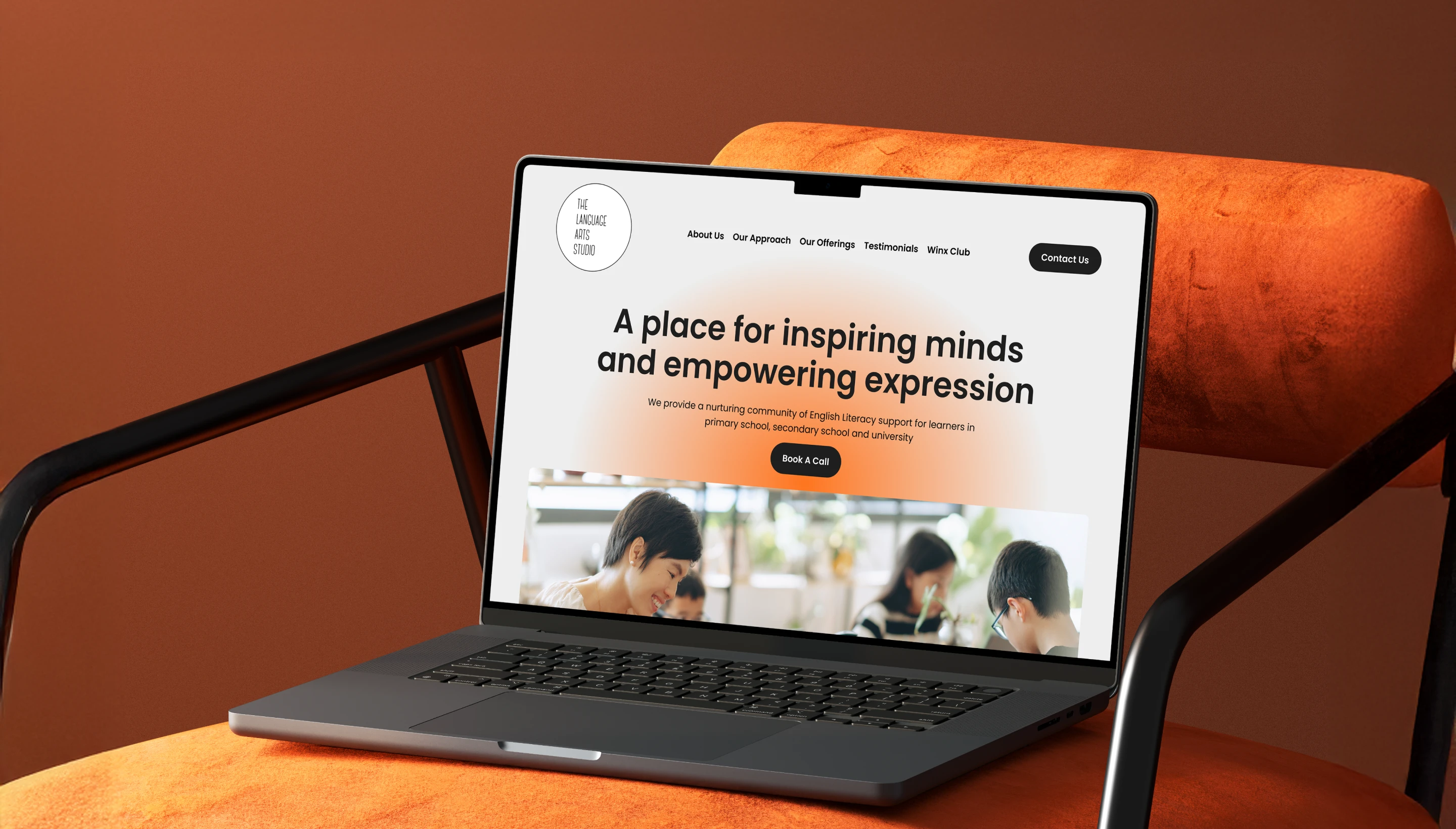 Laptop on an orange chair displaying a website homepage titled 'A place for inspiring minds and empowering expression' with navigation links and a call-to-action button.