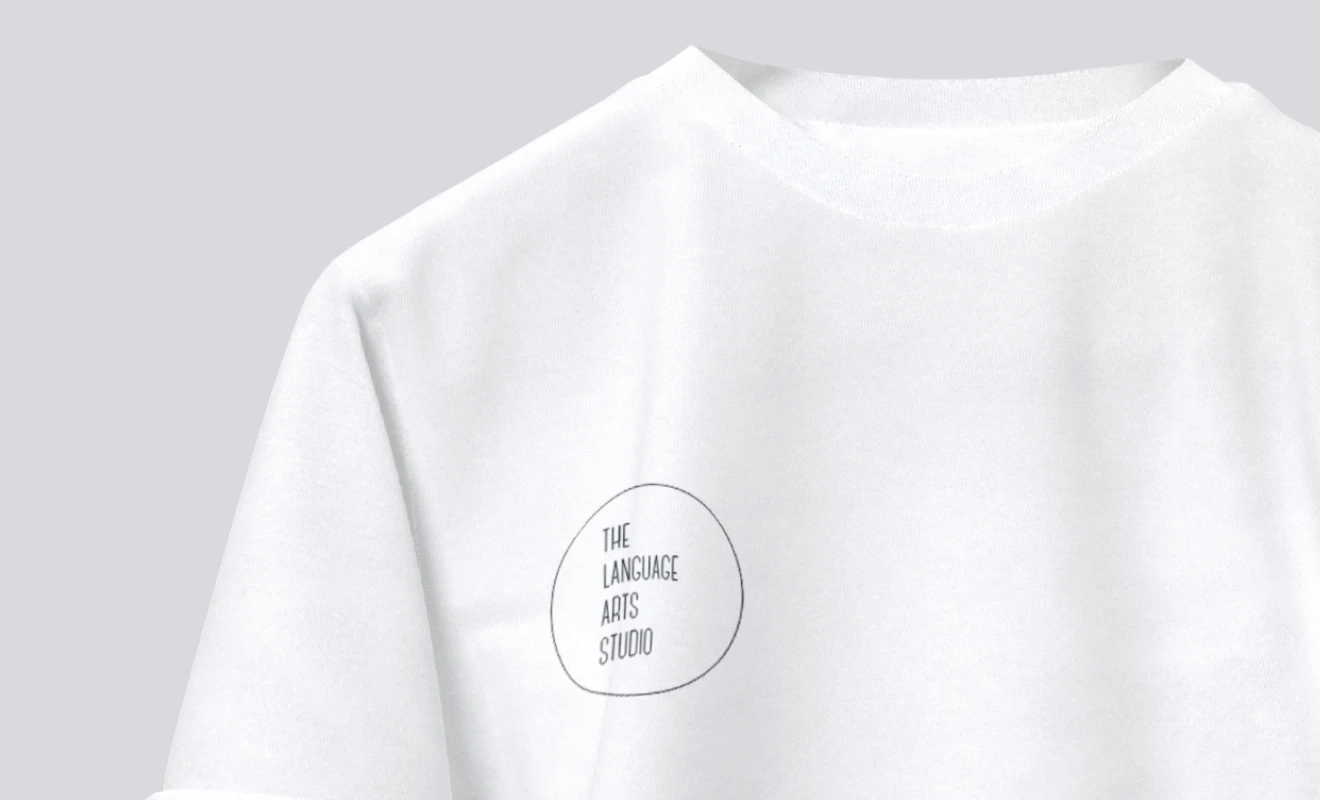 White T-shirt with a small black circular logo on the chest reading 'THE LANGUAGE ARTS STUDIO'.