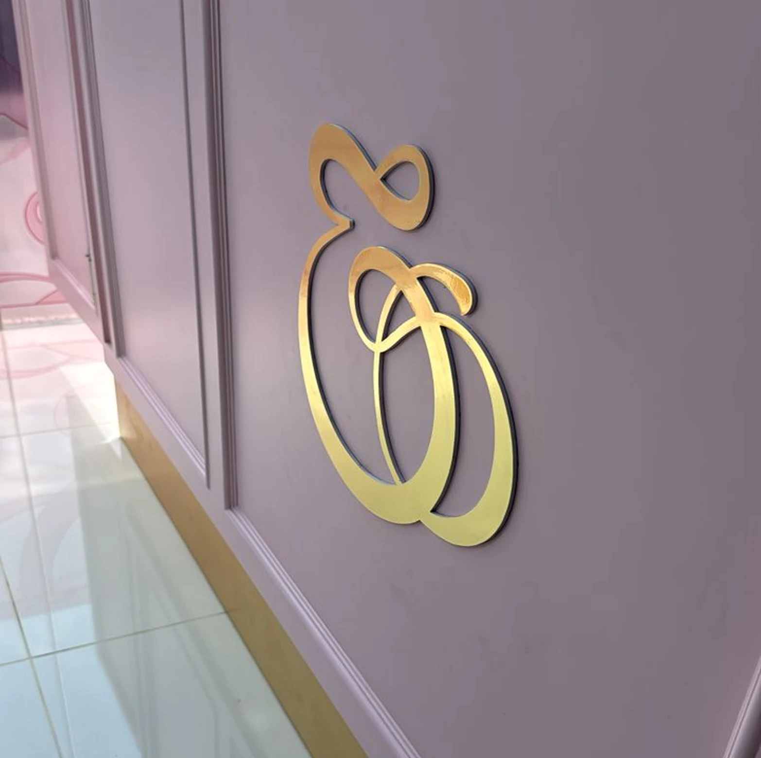 Gold decorative intertwined calligraphy mounted on a pink wall above a tiled floor.