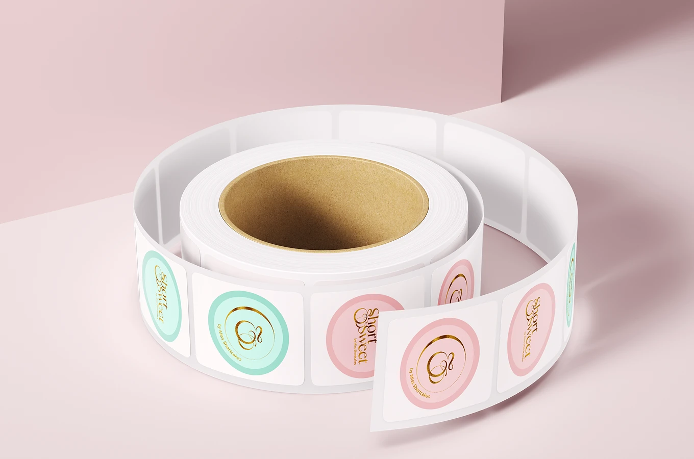 Roll of square labels featuring pastel pink and mint green circles with gold foil text and logos on a soft pink background.