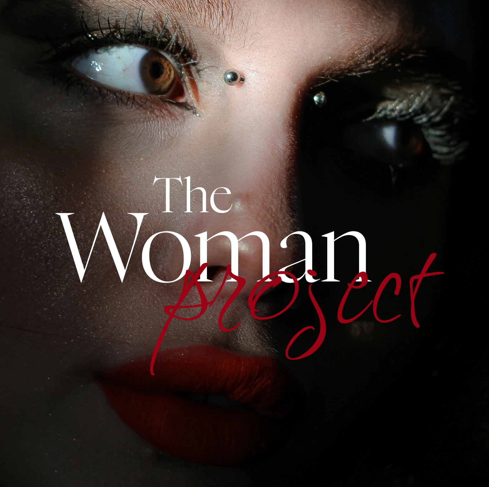 Close-up of a face with brown eyes, red lipstick, and two metallic nose piercings under dim lighting.