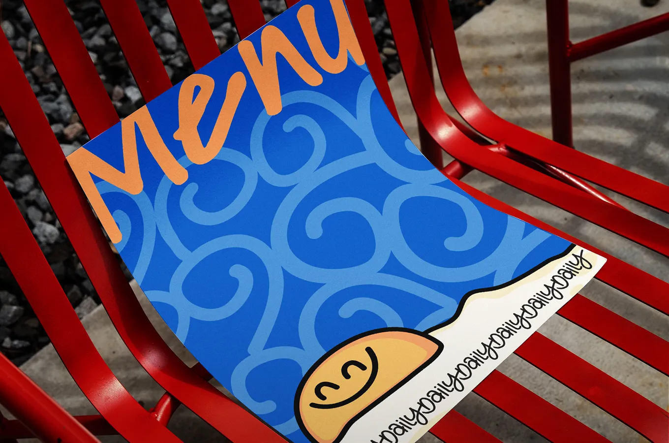 Colorful menu with blue swirls and a smiling orange dumpling illustration, placed on a red metal chair outdoors.