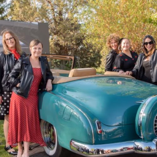 A group of women standing next to an old car.