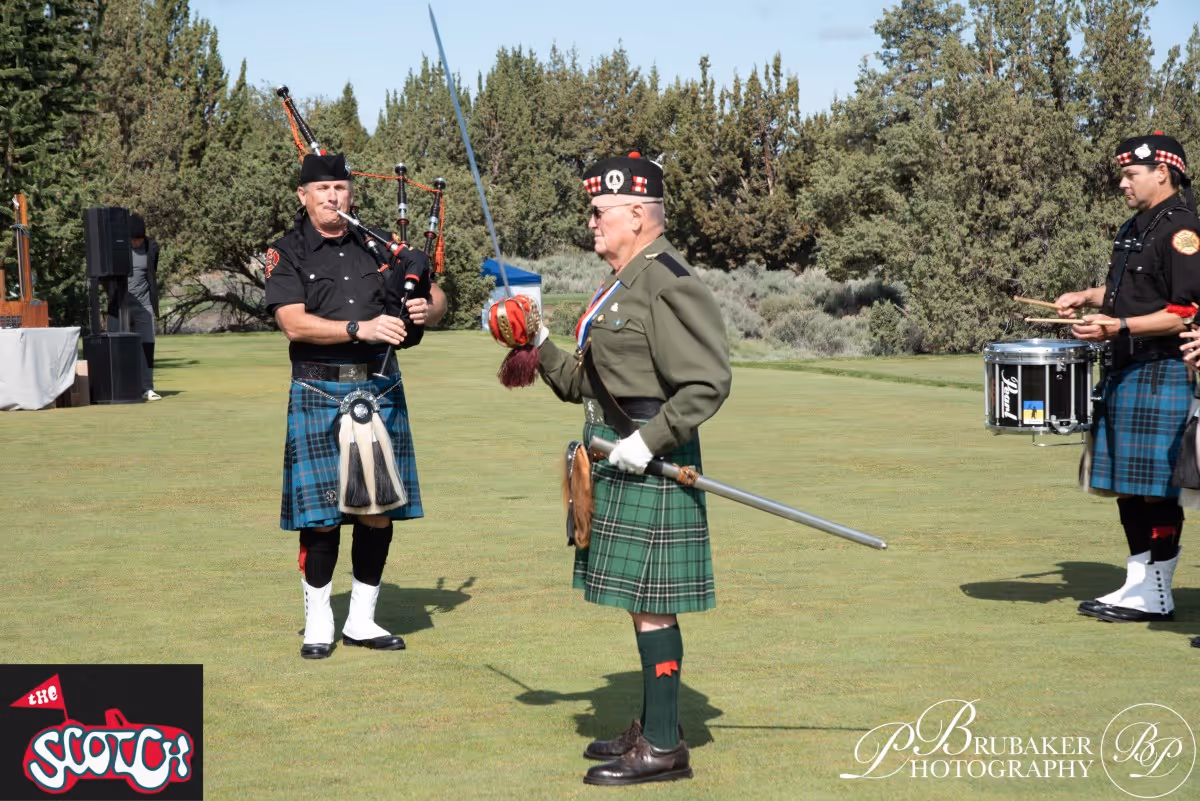 A group of men in kilts standing on top of a field.